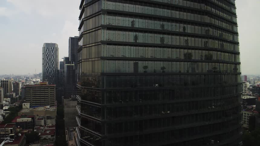 An aerial shot slowly pulls back from a futuristic, dark glass skyscraper overlooking a bustling city