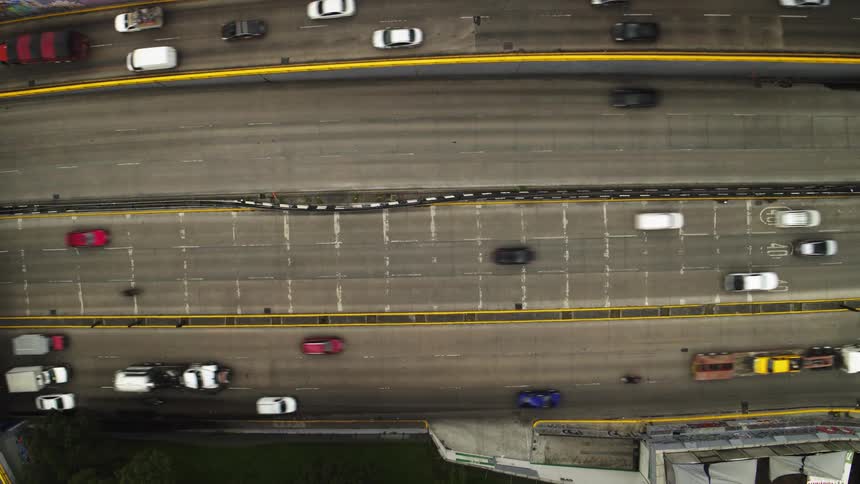 A top-down timelapse view of cars with motion blur speeding along a busy multi-lane highway in the city