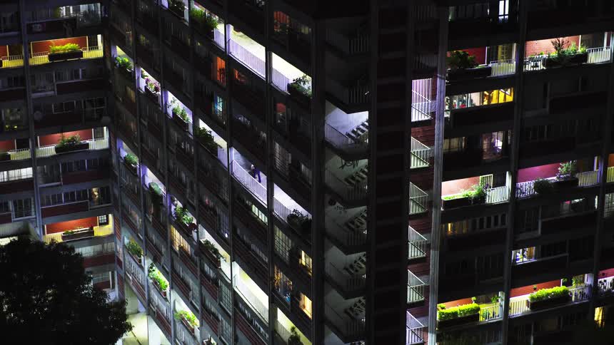 Zoom out time-lapse of a massive apartment complex at night, with lights flickering on and off in the windows