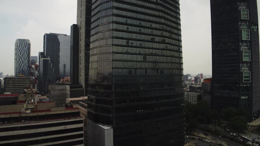 Aerial view slowly pushing towards a modern glass skyscraper in the financial district of Mexico City on a cloudy day