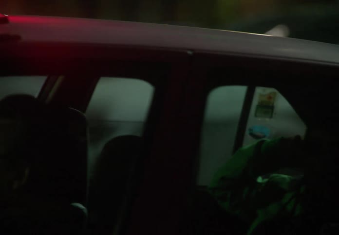 Close-up on a glowing red taxi sign as the car, with a driver and passenger inside, moves through the city streets at night