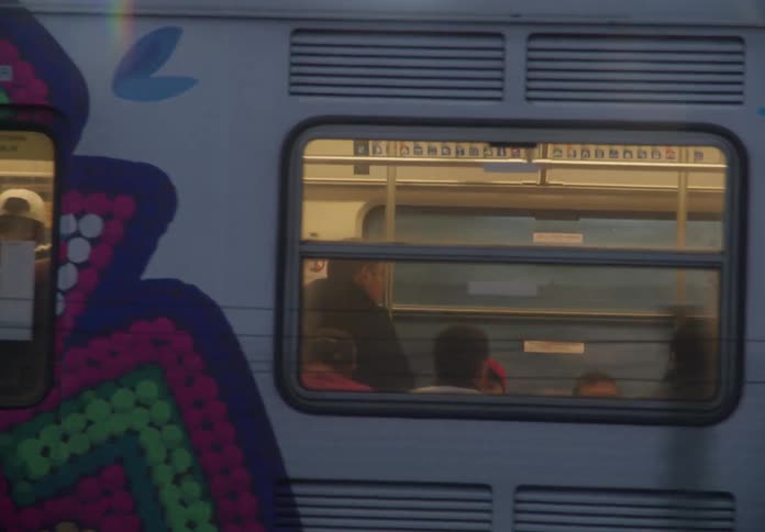 A colorfully decorated metro train filled with passengers travels through Mexico City at dusk