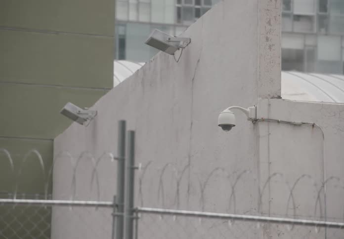 A quick zoom from a closed city street to a security camera mounted on a wall topped with barbed wire