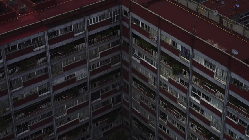 A slow high-angle zoom reveals a solitary figure on the balcony of a vast, repeating apartment complex