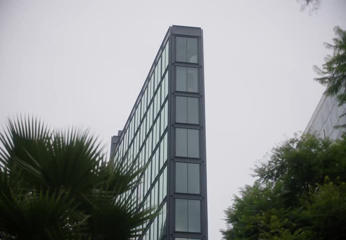 A slow upward tilt shot of the sharp, modern architecture of a glass skyscraper framed by trees on an overcast day