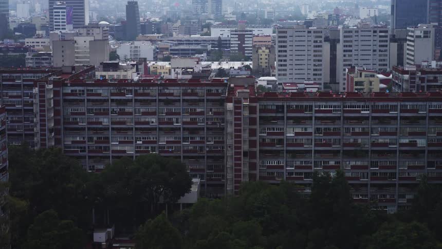 Slowly zooming out from a massive residential complex to reveal the sprawling, hazy cityscape in the background on a cloudy day