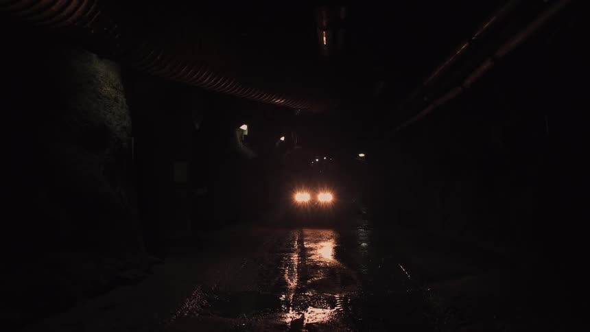 A truck is driving down a dark tunnel with its lights on