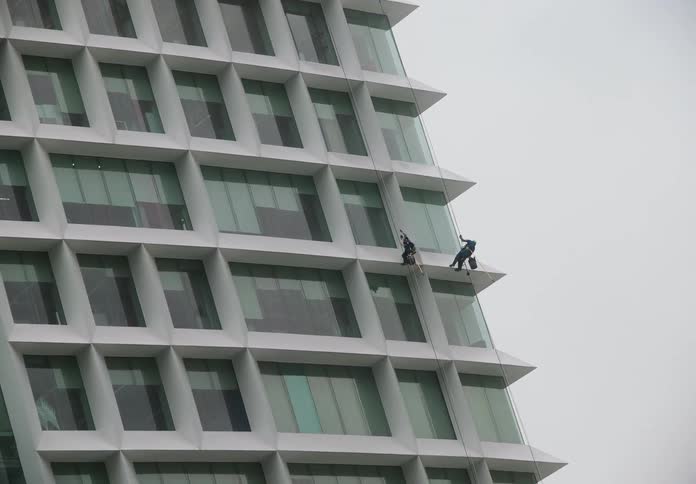 A team of two window washers rappel down the side of a modern office building to clean the exterior glass