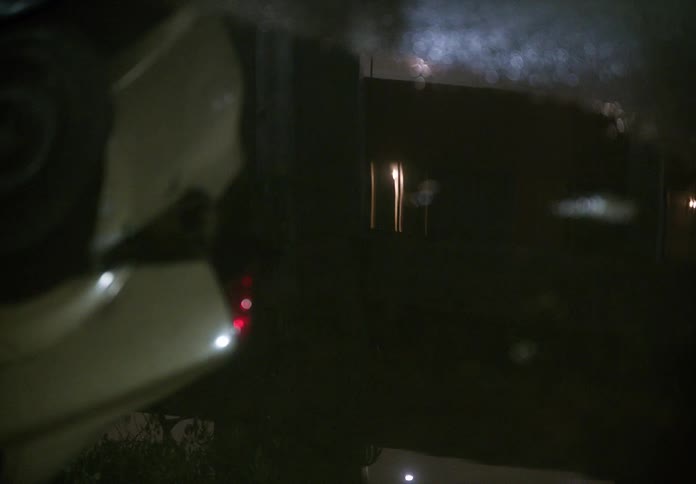 A blurry reflection of city lights and a passing car ripples in a puddle during a rainy night
