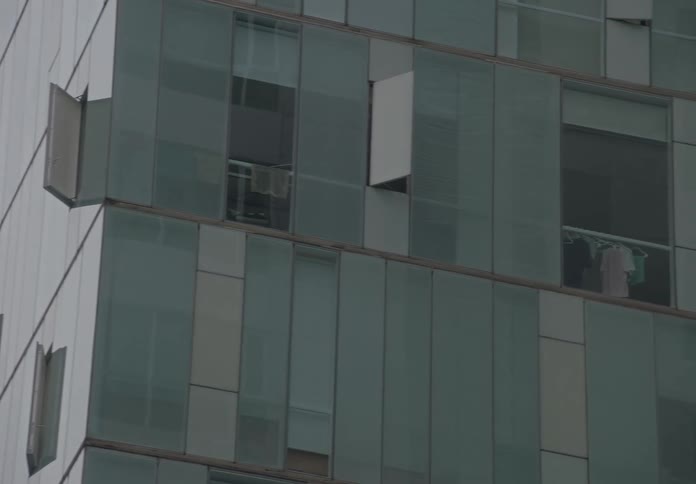 A slow pan reveals the modern glass facade of a residential building with unique open windows and laundry drying inside