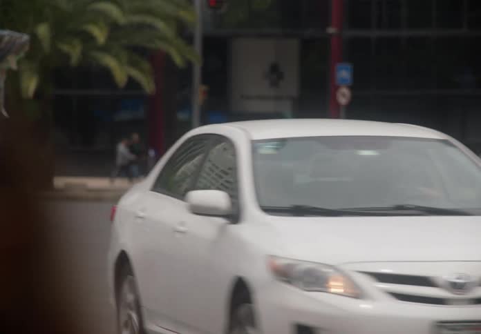 A white sedan and a pickup truck turn at a city street intersection on an overcast day