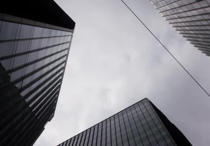 A low-angle view of modern skyscrapers with reflective glass facades zooms in on the cloudy grey sky above