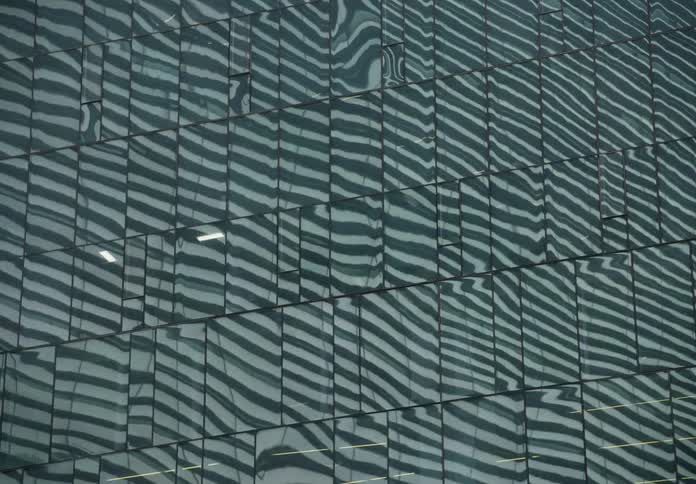 A rack focus shot reveals a modern glass building with an abstract, wavy reflection on its facade