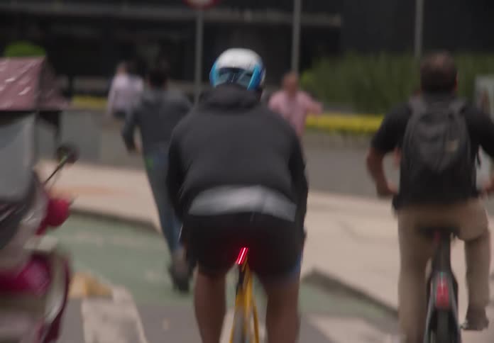 Motion-blurred tracking shot of diverse commuters on bicycles, scooters, and on foot navigating a busy city street