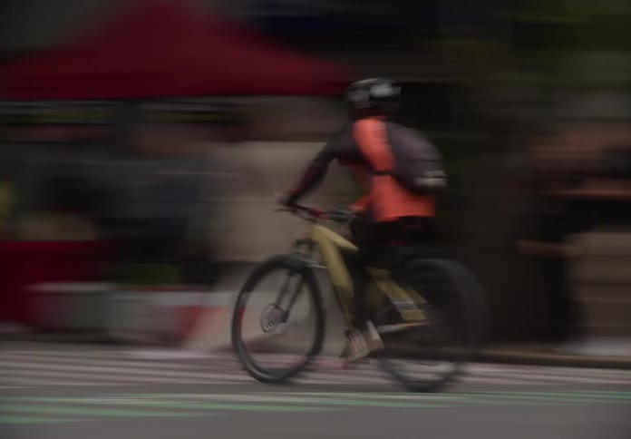 Motion blur side tracking shot of a cyclist wearing a helmet and backpack riding through the city