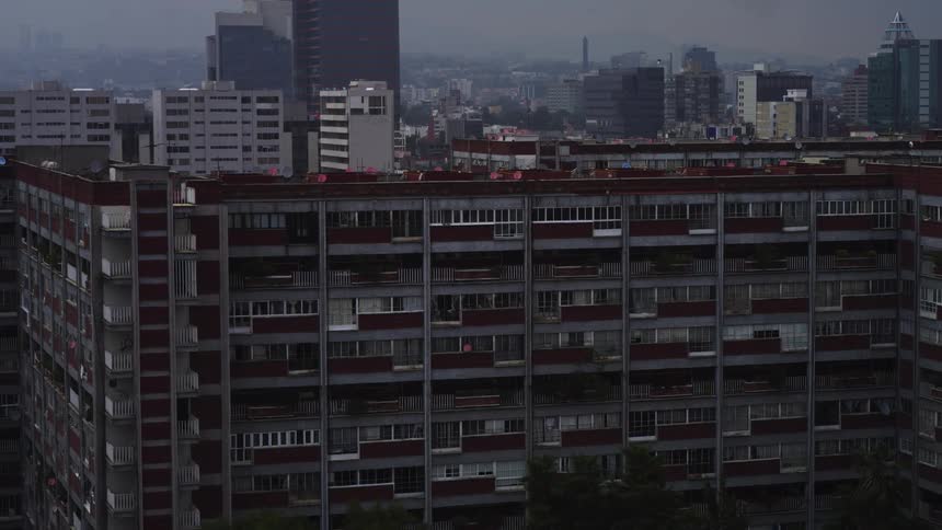Gloomy aerial shot pans left across a large, weathered apartment block in a vast, hazy metropolis