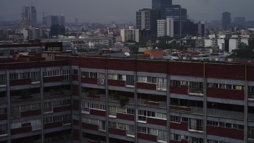 A slow aerial zoom-out reveals a sprawling cityscape with a large apartment complex in the foreground on a gloomy, overcast day
