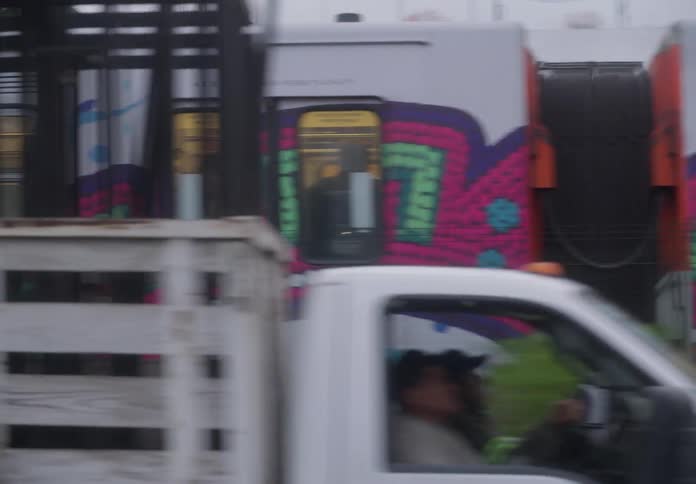 A side-view tracking shot of a colorful metro train in motion, with passengers visible through the windows