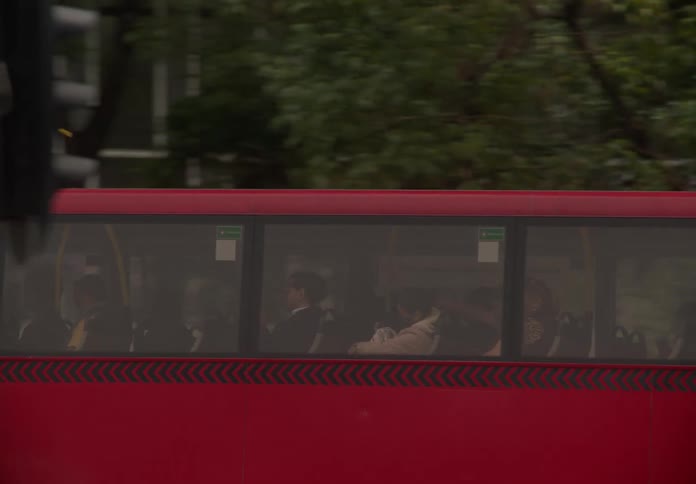 Passengers commute on a red public transportation bus as it drives through the city streets in slow motion