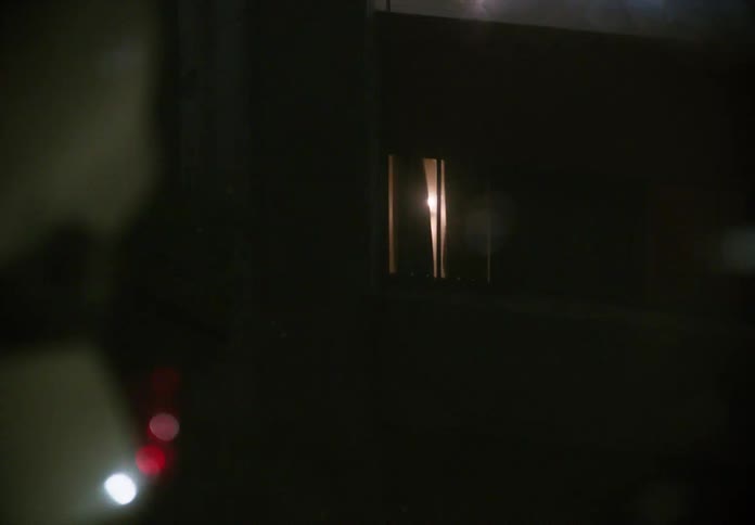 A pull-out shot reveals the reflection of a crashed, overturned car in a puddle on a dark, wet night