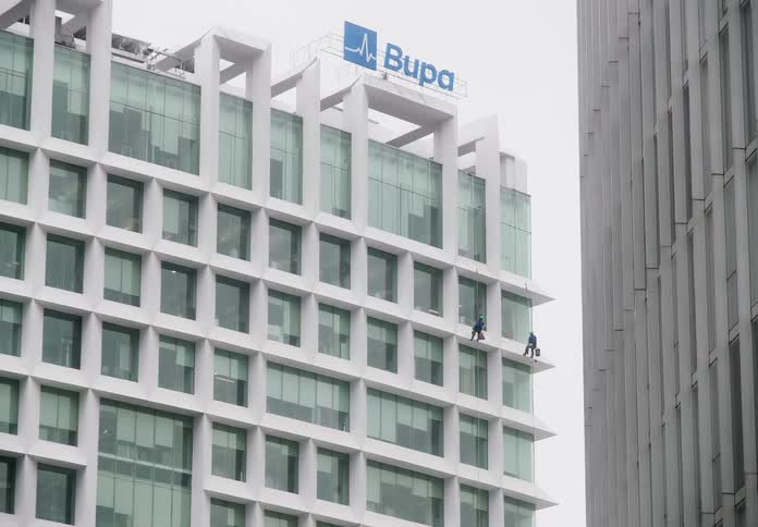 A slow zoom out reveals two professional window cleaners suspended by ropes as they work on a modern white corporate skyscraper
