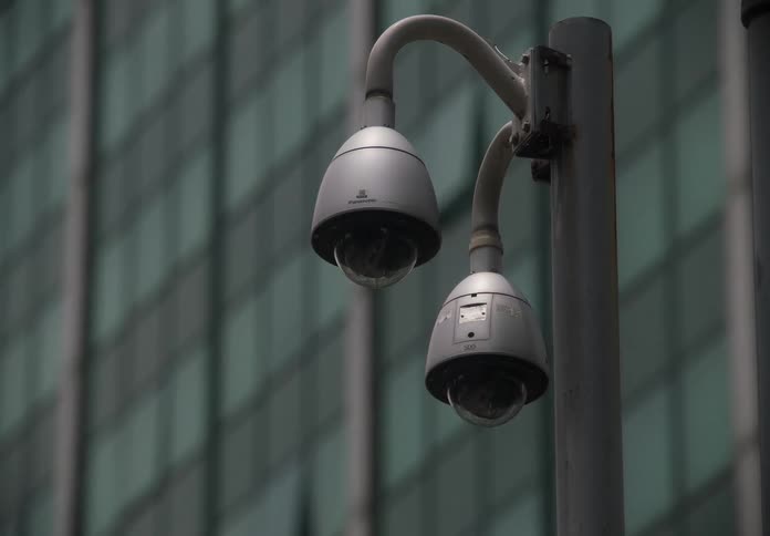 A close-up shot of two CCTV surveillance cameras on a pole with a modern building in the background