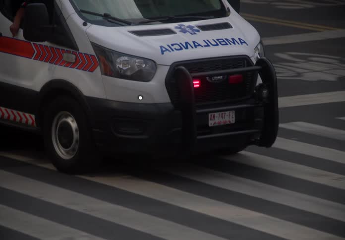A Mexican ambulance with flashing lights on drives through a city intersection in slow motion