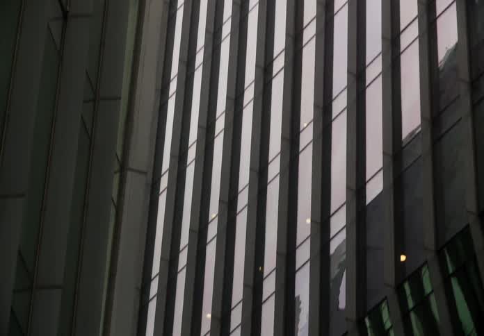 A slow tilt down reveals the striking vertical lines and geometric patterns of a modern glass skyscraper