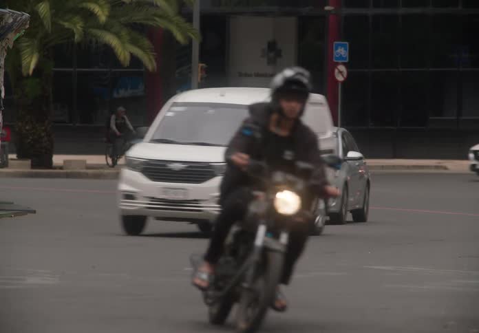 Slow-motion of city traffic, including cars and motorcycles, passing an intersection in front of the Mexican Stock Exchange building