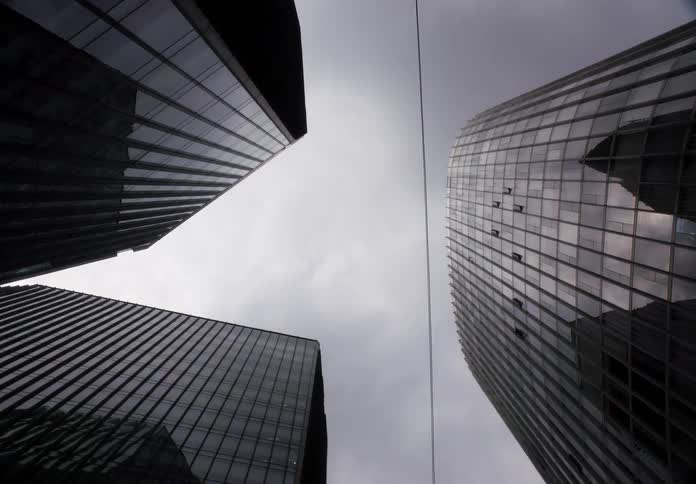 A dramatic low-angle time-lapse shows clouds moving across a grey sky and reflecting in the glass walls of modern city skyscrapers