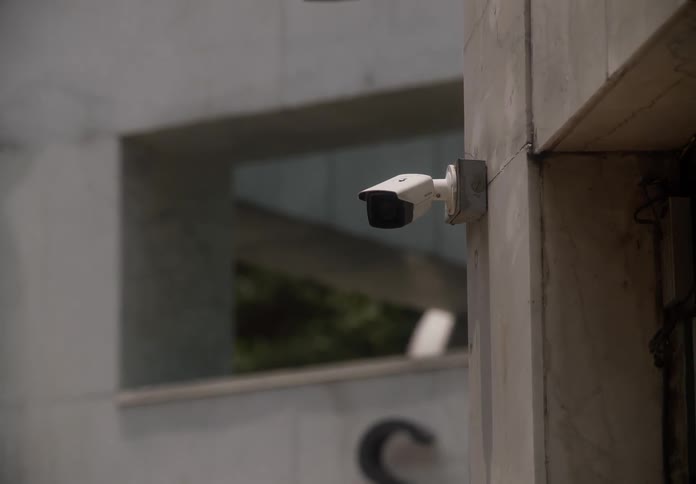 A slow zoom out reveals a white security camera mounted on the exterior of a modern building