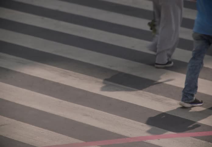 High-angle slow-shutter view of anonymous pedestrians and a motorcyclist crossing the bold stripes of a city crosswalk