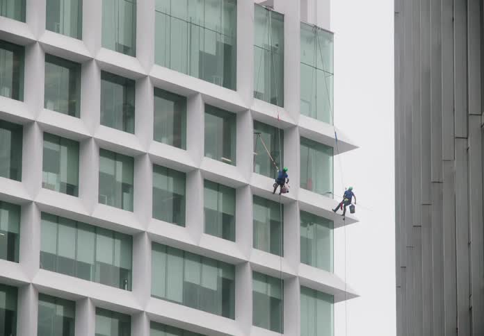 Tilting up the facade of a modern, white high-rise building to reveal a team of window washers rappelling down to clean the glass exterior