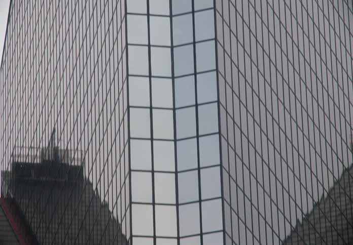 A slow tilt-down shot reveals the modern glass facade of a corporate skyscraper against an overcast sky