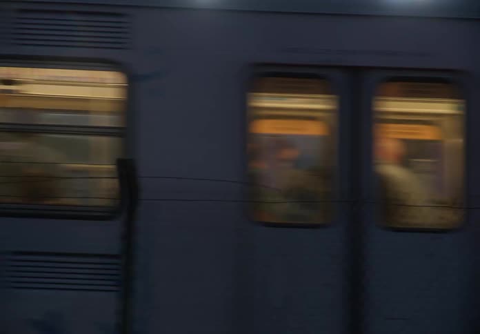 A commuter train with graffiti passes a building with a glowing hotel sign at dusk