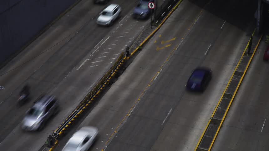 An aerial time-lapse view shows the blurred motion of cars driving on a busy city highway