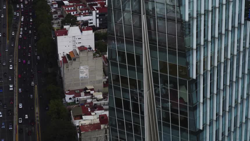 A high-angle aerial view of a busy city highway next to a modern glass skyscraper and older residential buildings