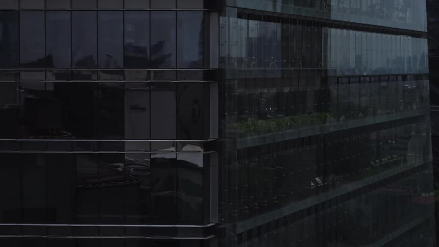 A slow aerial zoom out from a modern glass skyscraper reflecting the cityscape on an overcast day