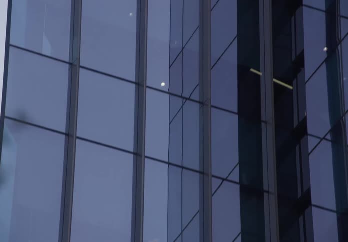 Slow upward tilt on a glass skyscraper, revealing the warped and distorted reflection of another modern building