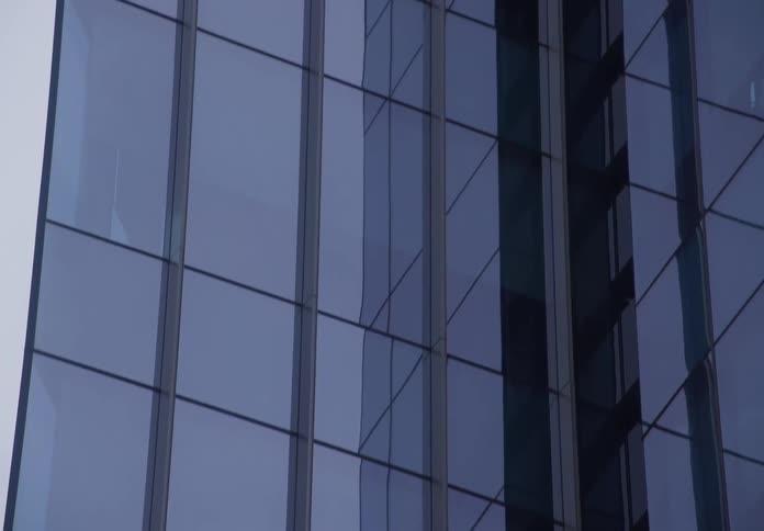 Slow tilt up shot of a modern glass skyscraper with reflections of the city and an overcast sky