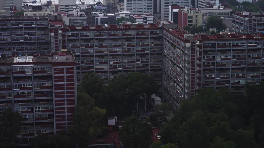 Time-lapse of a large, brutalist-style apartment complex nestled among green trees with the cityscape in the background