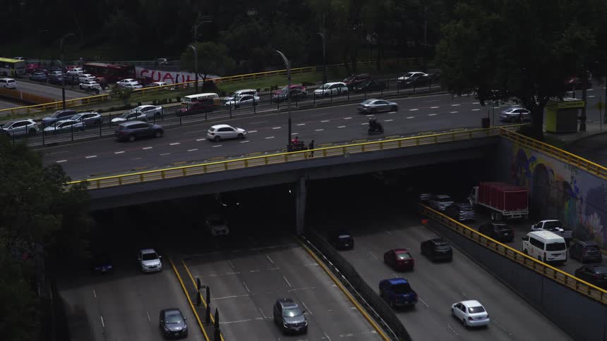 Static wide shot of a busy urban highway interchange with traffic moving on an overpass and through a tunnel below