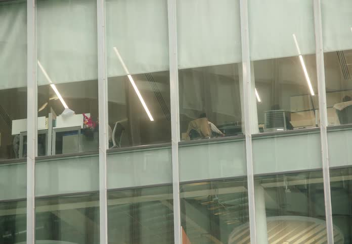 A slow zoom into the windows of a modern office building reveals employees working at their desks