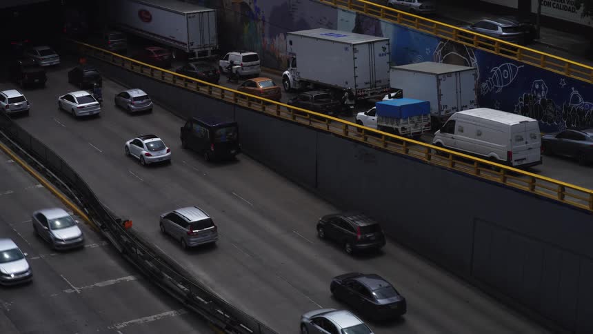 A high-angle view shows slow-moving cars and trucks on a congested urban highway next to graffiti-covered walls