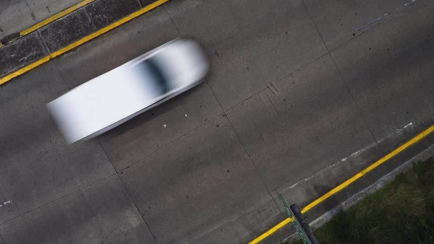 An overhead time-lapse captures the blurred motion of cars and trucks speeding along a busy highway
