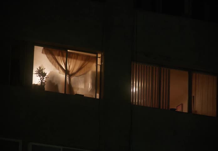 A view of two windows of an urban apartment building at night with lights on inside