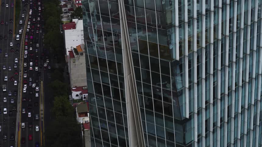 An aerial close-up on a modern glass skyscraper pulls back to reveal heavy traffic on the busy city highway below