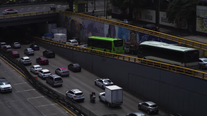 An elevated view captures slow-moving, congested traffic on a city expressway passing through a graffiti-covered underpass