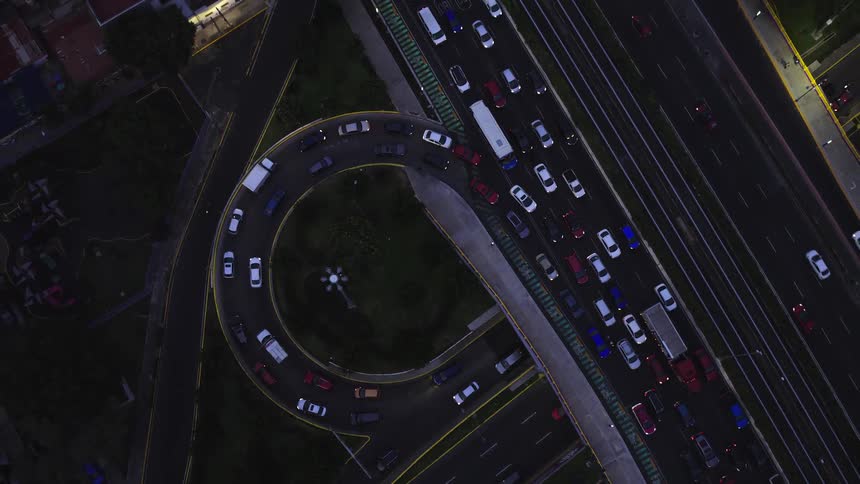 Ascending aerial top-down view of heavy traffic on a highway overpass and circular ramp at night
