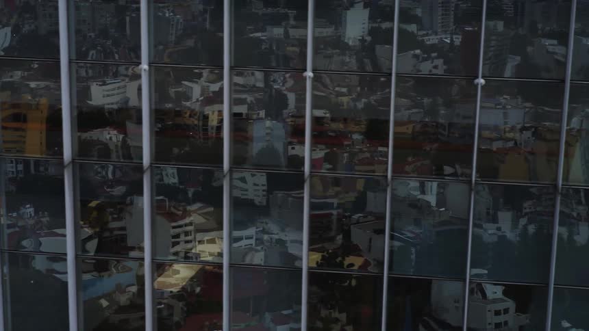 An aerial shot pans from the reflective glass facade of a skyscraper, showing the distorted city below, to reveal the adjacent Gentera corporate building